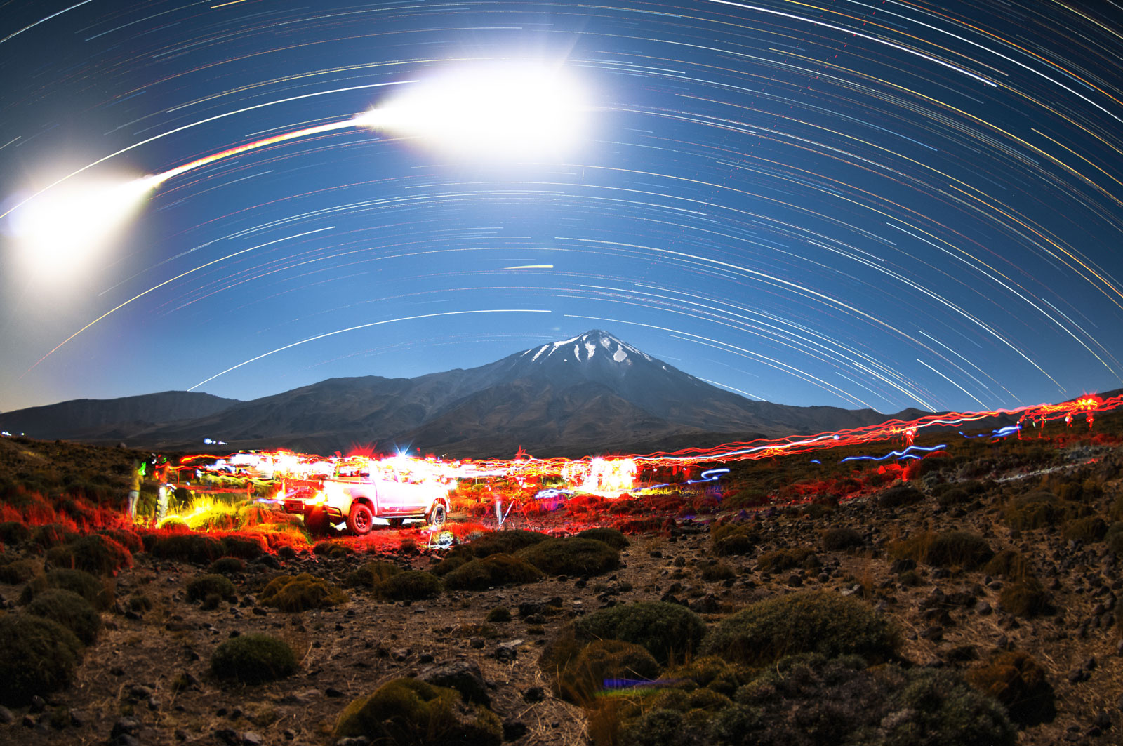 All-Sky Star Trails and Behind-the-Scenes: After nearly five hours under the stars on eclipse night, I created this single composite image that encapsulates the experience. The camera, armed with the Tokina AT-X 107 f/3.5-4.5 DX Fisheye (10-17mm) lens at 10mm, was left shooting continuously on a fixed tripod to record the trail of stars and the Moon’s path across the sky. The Moon's trail appears as a curved line whose intensity varies: dim during the total eclipse phase and brighter outside of it. Meanwhile, the foreground reveals a bit of the "backstage" of our photoshoot: the silhouettes and occasional lights of our small group of photographers can be seen, busy with cameras and gear amidst the landscape.